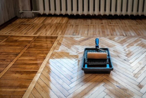 A paint roller on a tray placed on a freshly polished wooden floor with a herringbone pattern.